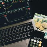A laptop displaying stock charts with Bitcoin, Euros, and a cellphone calculator, showcasing financial analysis.