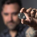 Adult male hand holding a Bitcoin, showcasing cryptocurrency focus indoors.