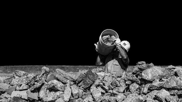 Black and white photo of a worker pouring rocks with a bucket in Mar del Plata, Argentina.